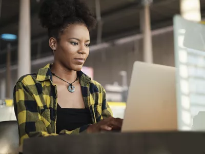 Woman sits on computer at a desk reading the Kraken review from coinsbase25